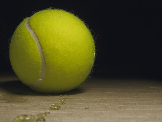 Close up of wet yellow tennis ball with black copy space and water droplets