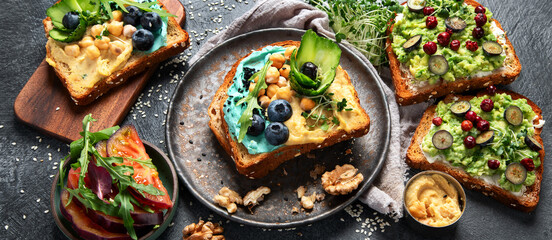 Vegetarian toasts with hummus, blueberry, avocado, tomato. delicious vegan breakfast on dark...