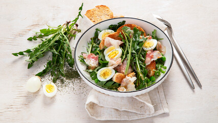 Summer fresh salad from dandelion leaves, eggs, bacon and with bread on light background