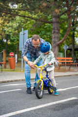 Young happy father teaches child daughter to ride public bike on one of traffic playground of Prague, Czech republic