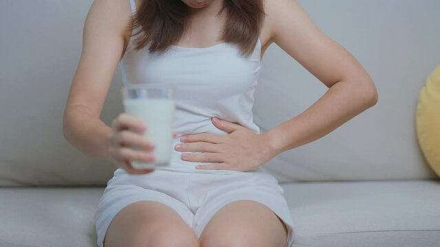 Lactose intolerance and Milk allergy concept. woman hold Milk glass and having abdominal cramps and pain when drink Cow Milk. Symptom stomach ache, Dairy intolerant, Nausea, Bloating, Gas and Diarrhea