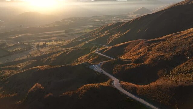 Road trip in New Zealand, winding road and beautiful sunset over the mountains. Aerial birds eye.
