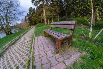 Wooden bench in the green park by the lake. Wide angle fisheye lens shot. Relaxation area in nature...