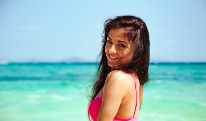 Naklejka premium Beautiful happy healthy woman with tanned body in pink swimsuit smiling in blue amazing island sea with brown long hair. Relaxing holidays. Sun summer seaside portrait