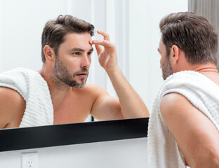 Middle aged hispanic man looking in mirror, facial skin and stubble. Male beauty care product....