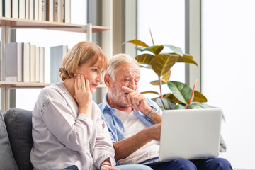 Caucasian man and a woman using laptop on a cozy sofa at home, Retired elderly family reading documents, Senior couple checking their bills