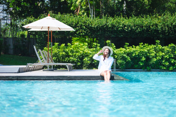 Portrait image of a woman with hat sitting and soaking legs by the swimming pool