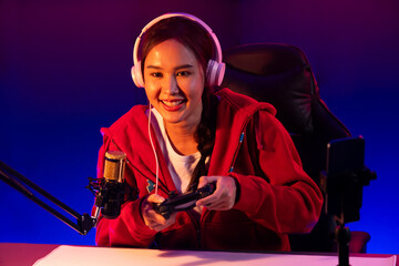 Host channel of smiling beautiful Asian girl streamer with joystick playing online game wearing...