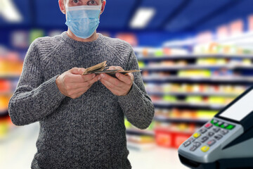 Man wearing medical mask with cash money going to make payment at self-service checkout. Effortless payment: Cash dollars exchanged at supermarket self-service terminal for seamless transactions