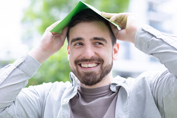 young man having a green paper as roof - obrazy, fototapety, plakaty