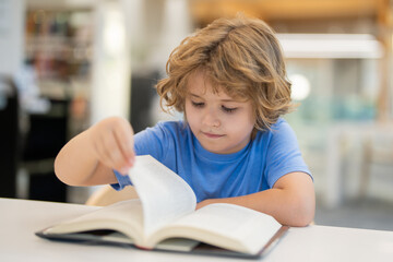 Fototapeta premium Kid reading book. Child reading book in school library. Learning from books. School education. Back to school Child reading book in a public library.