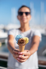 Happy, smiling woman holding ice cream cone with colorful ice cream balls. Sunny sea coastline at...