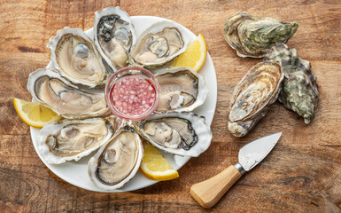 Opened raw oysters with sauce and lemon slices on plate on wooden table. Top view. © volff