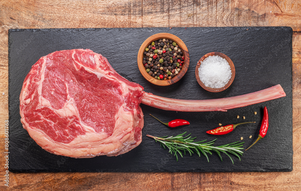 Wall mural Raw rib steak with bone or tomahawk steak with seasonings on slate serving plate. Flat lay.