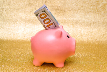Piggy Bank with the US currency stands on a shiny Golden background.
