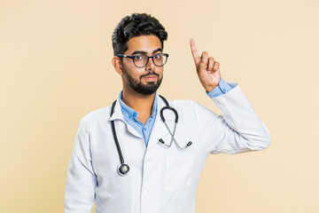 Eureka. Inspired Indian young doctor cardiologist man pointing finger up with open mouth, having good idea, plan, startup, inspiration motivation solution. Apothecary pharmacy guy on beige background
