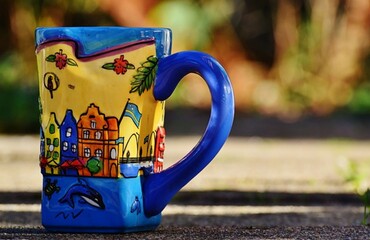 There is a colorful mug with a painting of the city, and it is placed on the ground in the street,...