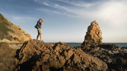 Young photographer standing on a rock cliff taking pictures of the landscape. travel and adventure...