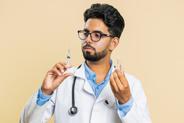 Indian young doctor cardiologist man holds syringe needle and ampoule tube with medical vaccine...