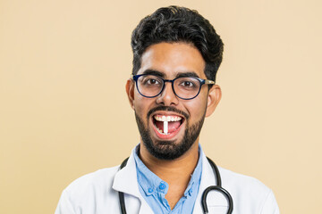 Smiling Indian Hindu doctor man puts of tablet pill white capsule into mouth, recommends drugs immunization cure treatment. Health care. Vitamins for joints, hair, skin, nails. Apothecary pharmacist