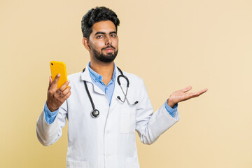 Indian doctor cardiologist man using smartphone showing pointing empty place, advertising...