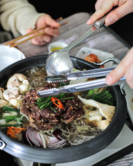 A person uses ladles and chopsticks to serve a stew containing beef, mushrooms, onions and...