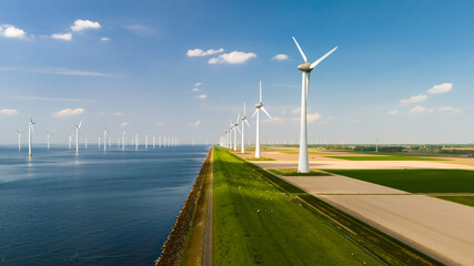 A line of majestic wind turbines stand tall next to a tranquil body of water, harnessing the power...