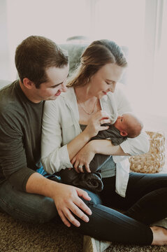 Dad and mom sitting close looking at newborn baby held in moms arms