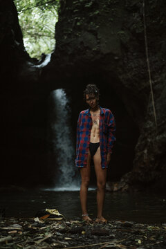 A young woman puts on clothes after swimming in a waterfall.