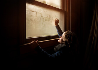 Happy child writing thankful on window sill