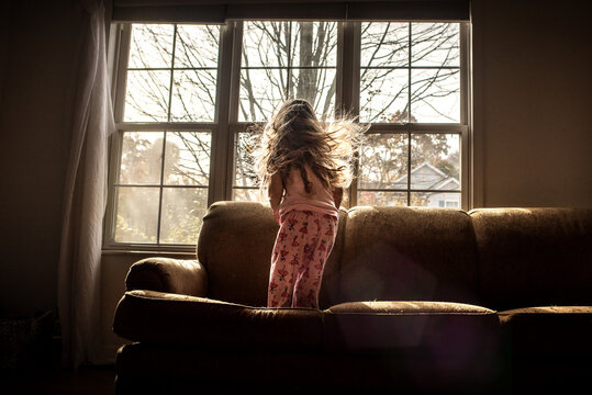 Little girl with blonde curls looking out window in home