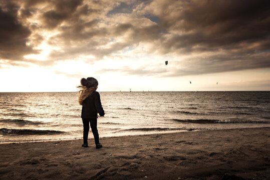 Young girl watching kite boarders at sunset