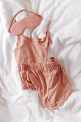 Pink female pajama and sleep eye mask on white cloth bed sheet. Top view comfort pyjamas for health...