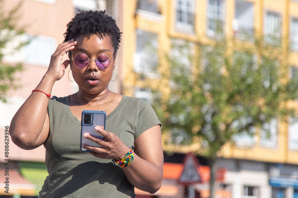 Wall mural black woman looking at mobile phone with surprise gesture on the street