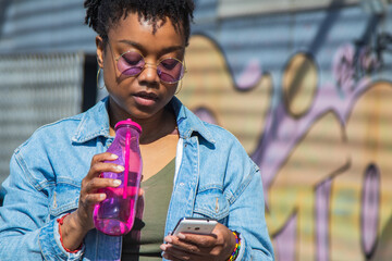 urban black woman looking at phone and drinking a soft drink on the street