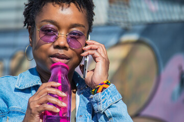 urban woman drinking a soft drink on the street while talking on the phone