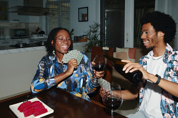Smiling Black couple drinking red wine and playing cards at home