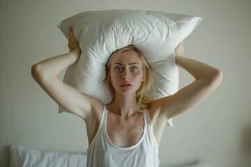 Young woman covering ears with pillow because of noise.