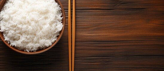 Top view of a wooden bowl filled with Jasmine rice accompanied by chopsticks on a grunge wood table...