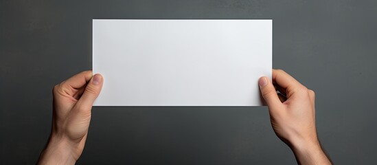 A male hand holding a blank paper sheet against a gray background leaving space for an image. Copy...