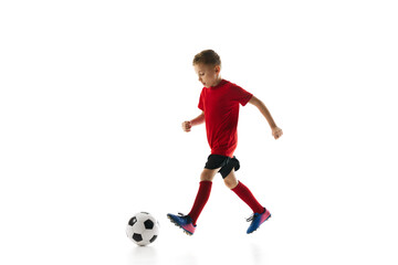 Little athlete boy, dribbling ball to take perfect goal against white studio background. Young soccer player in motion. Concept of professional sport, championship, youth league, hobby. Ad