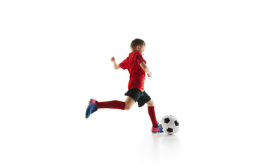 Sporty little boy, kicks ball to make perfect pass in motion against white studio background. Small football player makes goal. Concept of professional sport, championship, youth league, hobby. Ad