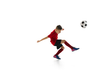 Little athletic boy with soccer ball doing flying kick in motion against white studio background. Dynamic portrait. Concept of professional sport, championship, youth league, hobby. Ad