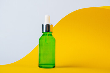 Green glass cosmetic bottle, Skin care or sunscreen cosmetic with stylish props on yellow and white background.