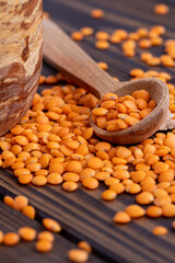 Photo of red lentils in wooden bowl with wooden measuring cup on wooden background.  Healthy lifestyle. Vegetarian and vegan diet.