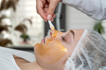 Woman enjoying soothing pampering golden facial mask by beautician at spa salon