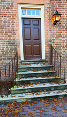 front door to brick house with a lantern. mossy concrete steps with autumn leaves at the entrance.