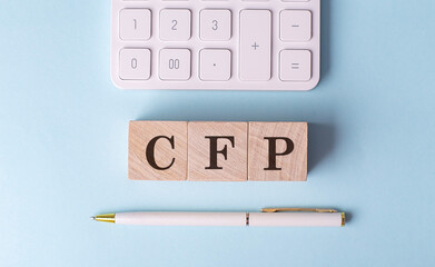 CFP word on wooden block with pen and calculator on blue background