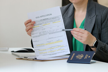 Close up of a woman holding a visa application paper document with an American passport laying on office table