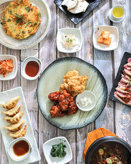 A variety of Korean food spread on a wooden table, including fried chicken, dumplings, a seafood...